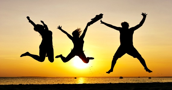 Three people jumping in silhouette on a beach at sunset