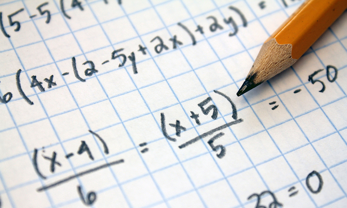 Math equations handwritten on graph paper beside a sharpened pencil